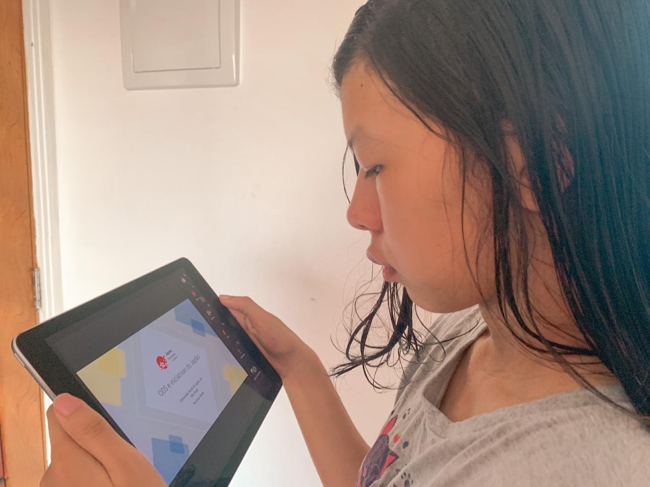 Uma menina assistindo as aulas do MONUEM em seu tablet. 